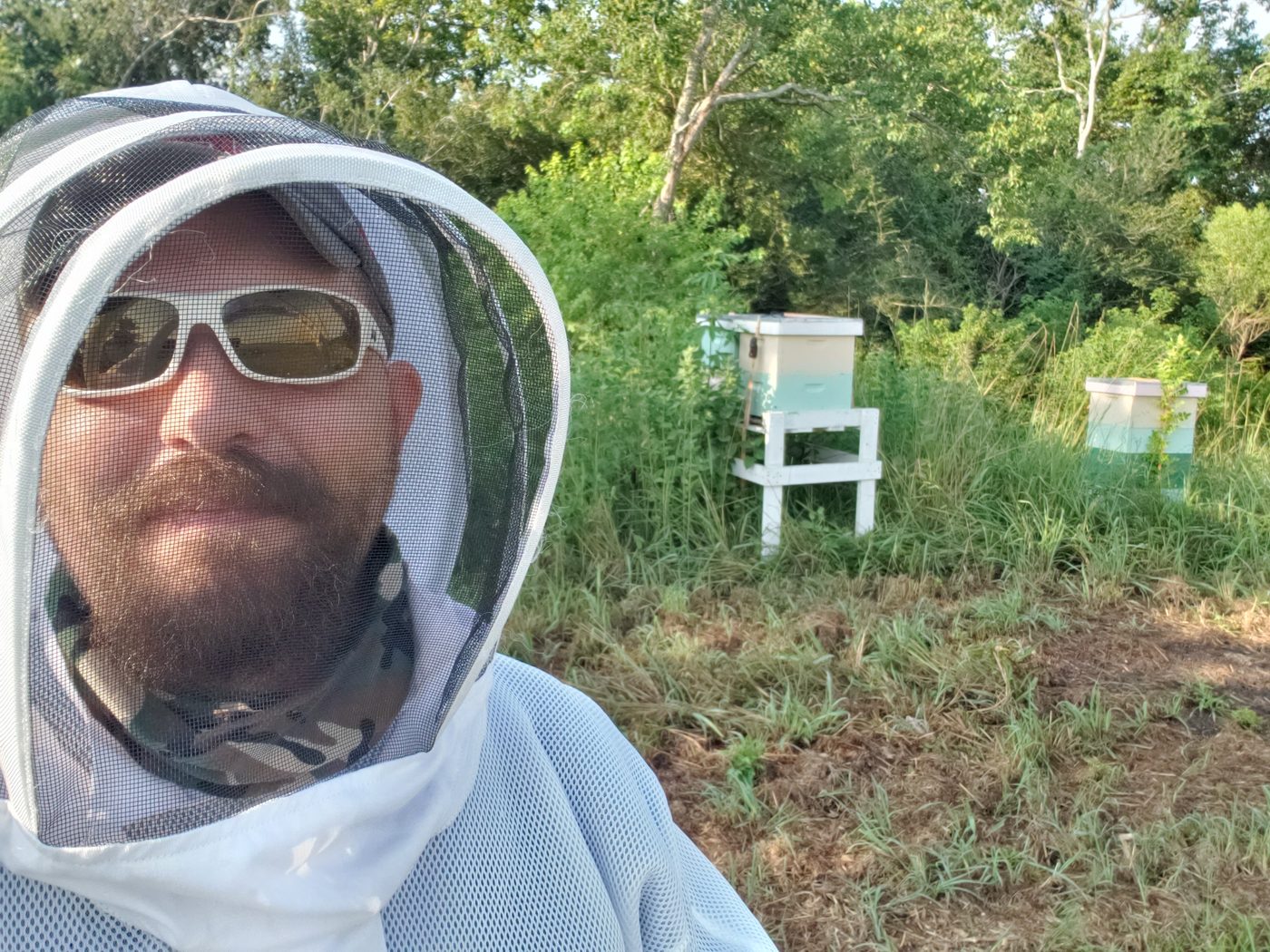 Beekeeper in veil smiling near white and teal hives